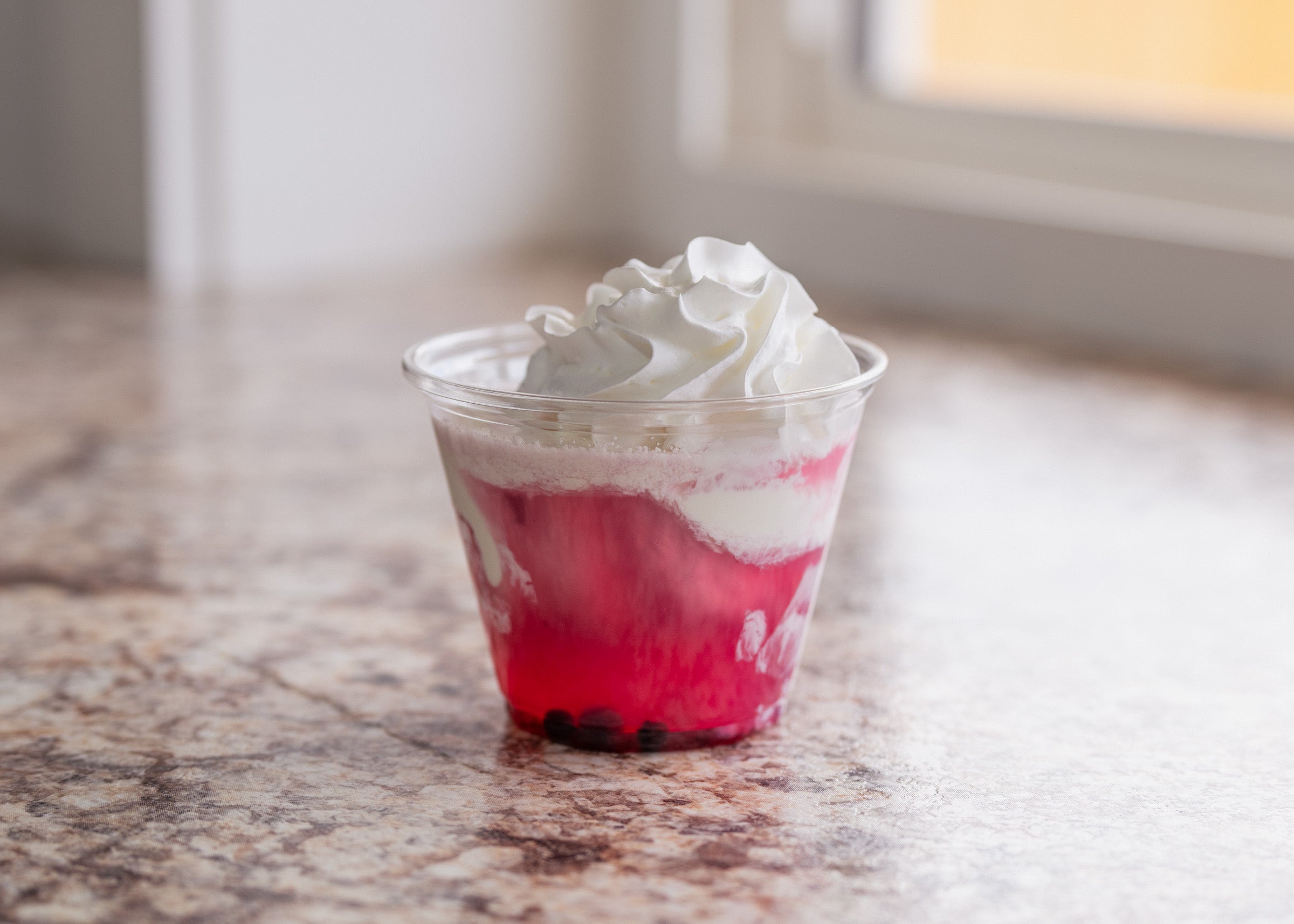 Clear plastic cup dessert with layered red fruit gelatin or jelly topped with whipped cream, served on a marble countertop at Lakeland Orchard