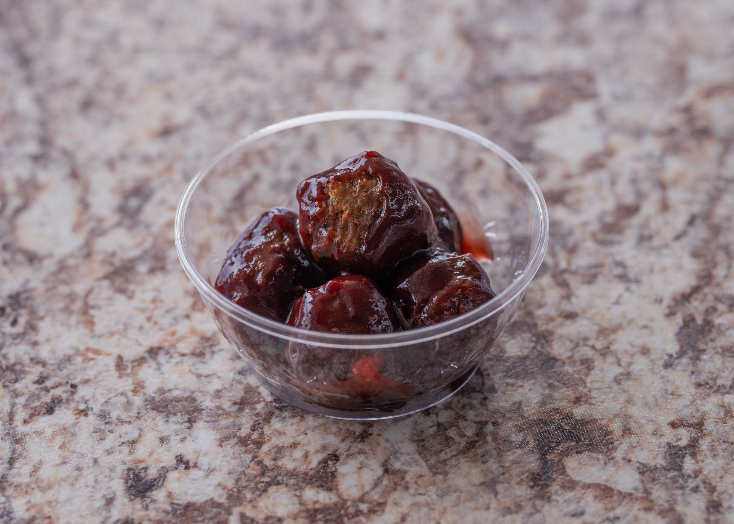 Clear plastic cup filled with barbecue glazed meatballs served on a marble countertop at Lakeland Orchard
